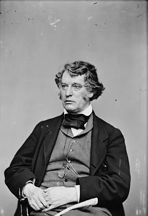 Fotografía antigua de Charles Sumner, sentado, con el pelo ondulado, patillas, chaleco y corbata de lazo, con unos papeles en las manos.